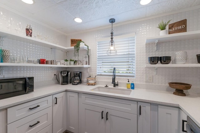 kitchen featuring dishwashing machine, sink, crown molding, white cabinetry, and decorative light fixtures