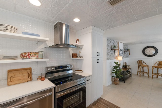 kitchen featuring white cabinetry, appliances with stainless steel finishes, tasteful backsplash, and wall chimney range hood