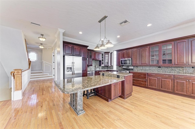 kitchen with appliances with stainless steel finishes, pendant lighting, a kitchen bar, a kitchen island, and tasteful backsplash