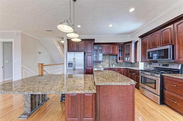 kitchen featuring a kitchen island, ornamental molding, appliances with stainless steel finishes, light wood-type flooring, and backsplash