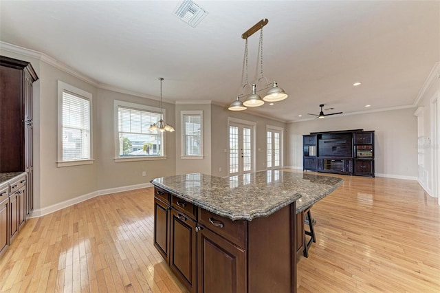 kitchen featuring decorative light fixtures, a center island, ceiling fan with notable chandelier, dark stone counters, and a breakfast bar