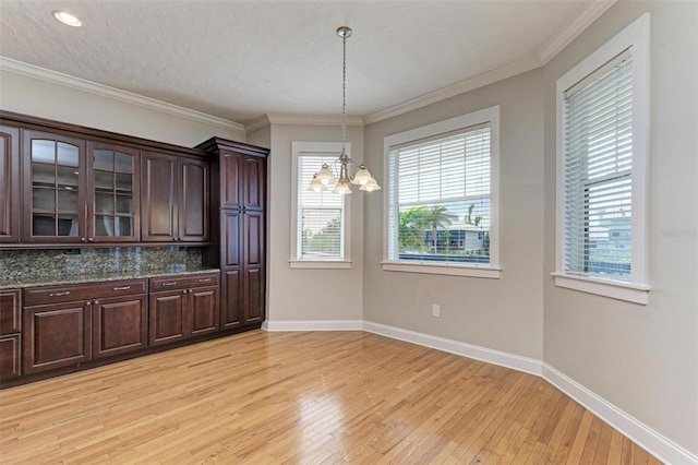 unfurnished dining area with a textured ceiling, an inviting chandelier, ornamental molding, and light hardwood / wood-style floors