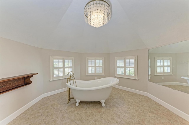 bathroom with lofted ceiling, a soaking tub, a notable chandelier, and baseboards