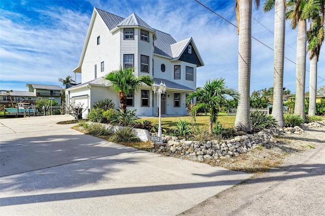 victorian home with concrete driveway, an attached garage, a standing seam roof, metal roof, and fence