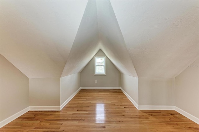 bonus room featuring lofted ceiling, light wood-style floors, baseboards, and a textured ceiling