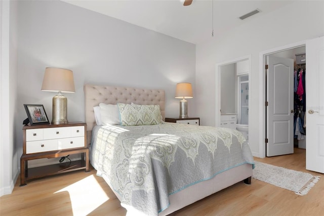 bedroom featuring a walk in closet, ensuite bath, light wood-type flooring, and ceiling fan