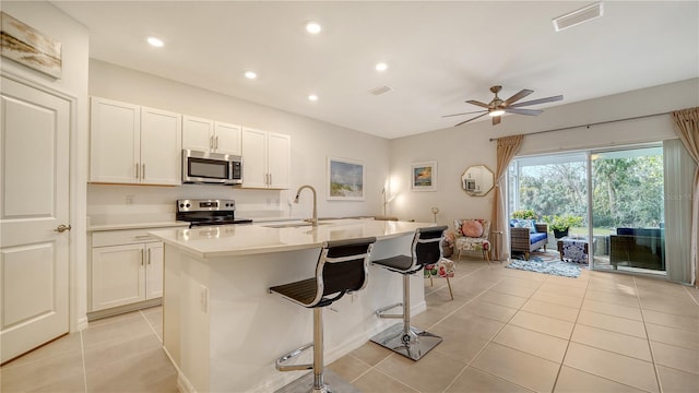 kitchen featuring an island with sink, white cabinetry, light tile patterned flooring, and stainless steel appliances