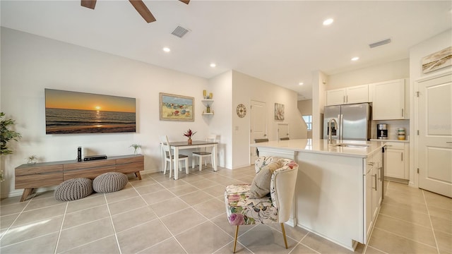 kitchen featuring stainless steel refrigerator with ice dispenser, white cabinetry, a center island with sink, and light tile patterned flooring