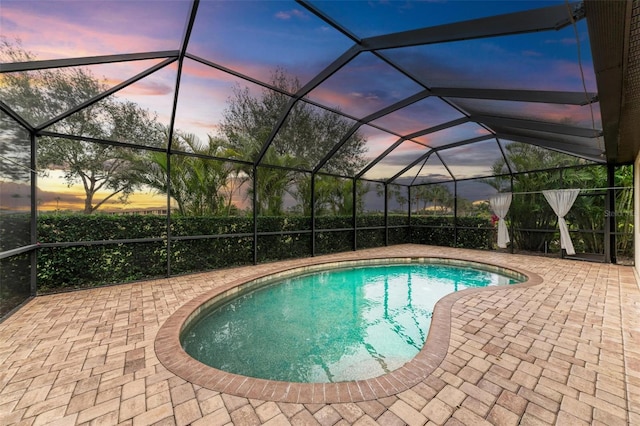 pool at dusk featuring a lanai and a patio