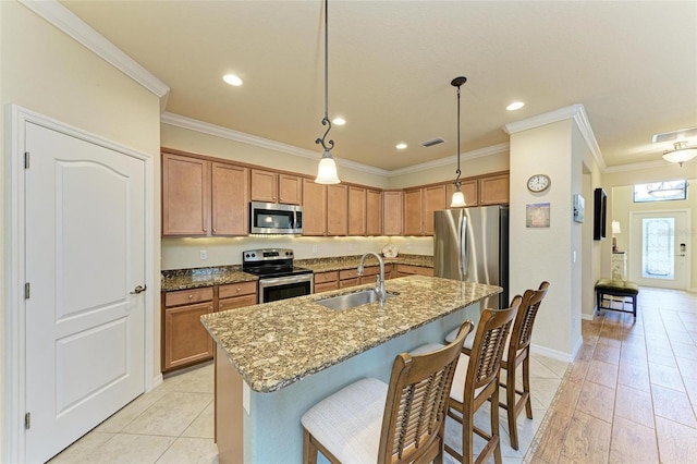 kitchen with pendant lighting, sink, appliances with stainless steel finishes, a kitchen island with sink, and stone countertops