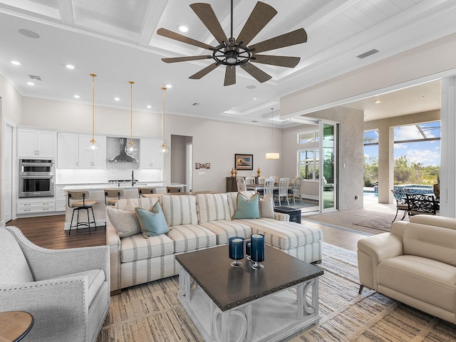 living room with ceiling fan, beam ceiling, coffered ceiling, light wood-type flooring, and ornamental molding