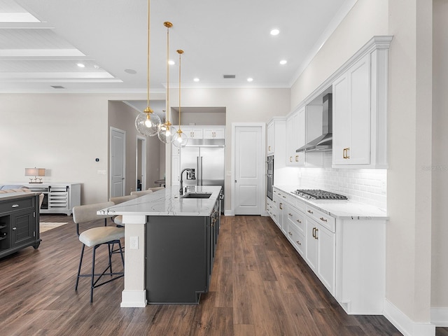 kitchen featuring wall chimney range hood, pendant lighting, a center island with sink, sink, and white cabinetry