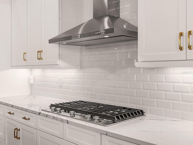 kitchen with stainless steel gas stovetop, white cabinetry, backsplash, light stone countertops, and wall chimney exhaust hood