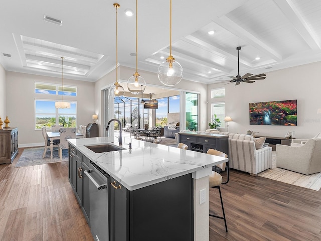 kitchen featuring a kitchen island with sink, dark wood-type flooring, hanging light fixtures, light stone countertops, and sink