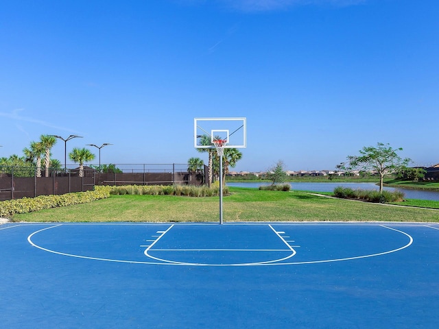 view of sport court with a water view and a lawn