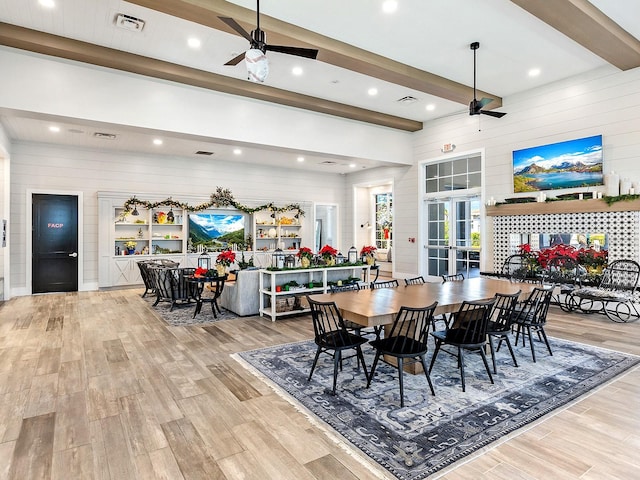 dining area featuring ceiling fan, beamed ceiling, wooden walls, and light hardwood / wood-style floors