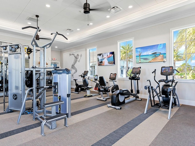 exercise room featuring ceiling fan, ornamental molding, light colored carpet, and a raised ceiling