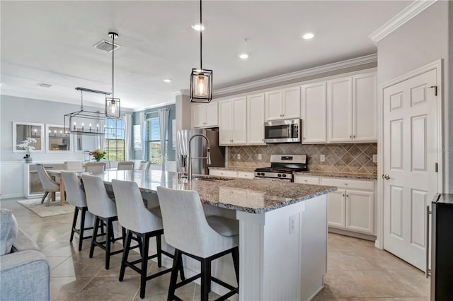 kitchen with stainless steel appliances, a center island with sink, white cabinets, and decorative light fixtures