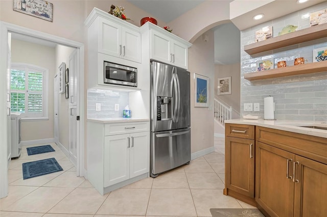 kitchen with appliances with stainless steel finishes, tasteful backsplash, white cabinetry, light tile patterned floors, and washer and clothes dryer