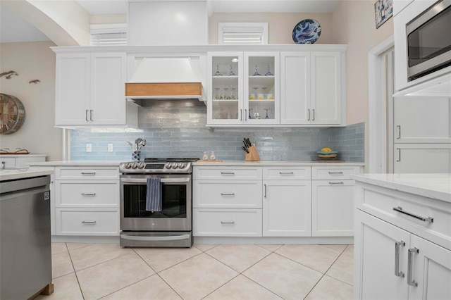 kitchen featuring premium range hood, appliances with stainless steel finishes, light tile patterned floors, and white cabinets