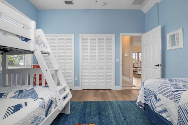 bedroom featuring multiple closets, lofted ceiling, wood-type flooring, and multiple windows