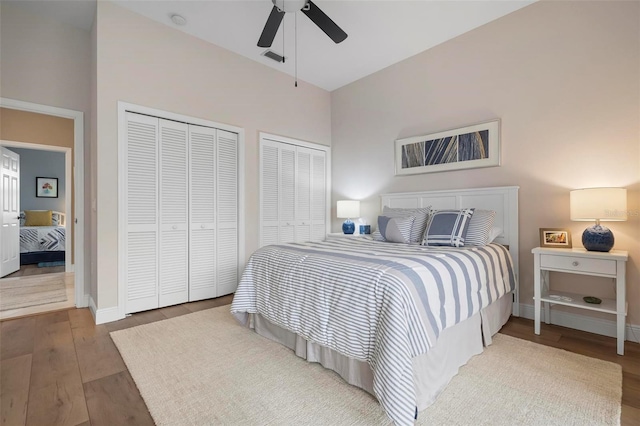 bedroom with ceiling fan, hardwood / wood-style floors, and two closets