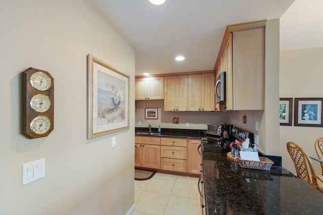 kitchen with light tile patterned flooring, dark stone countertops, light brown cabinets, and sink