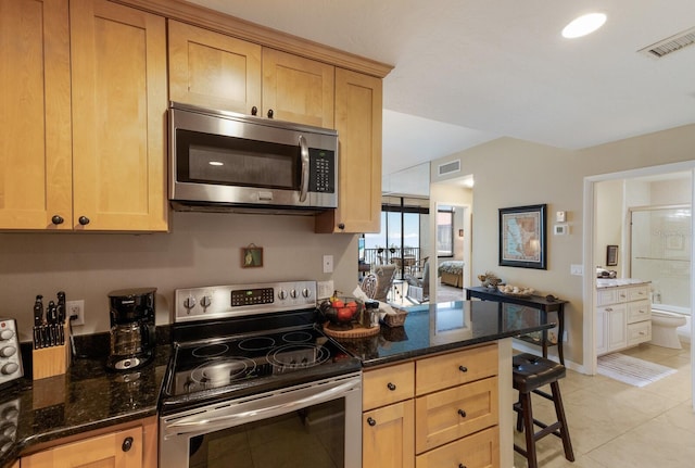 kitchen with a kitchen breakfast bar, light tile patterned floors, stainless steel appliances, and dark stone countertops