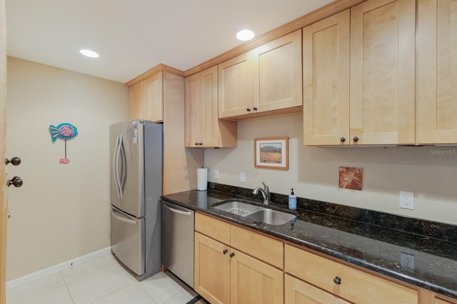 kitchen with stainless steel appliances, light brown cabinets, light tile patterned flooring, dark stone countertops, and sink