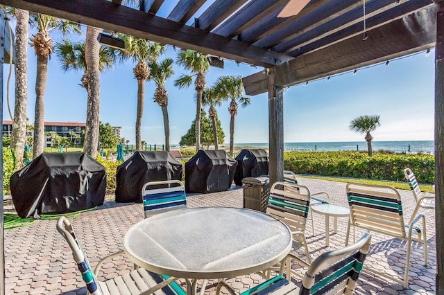 view of patio with grilling area, a water view, and a pergola