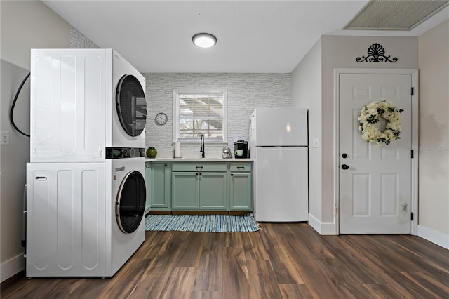 laundry room with sink, stacked washer / drying machine, dark hardwood / wood-style flooring, and cabinets