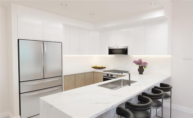 kitchen featuring sink, white cabinetry, a breakfast bar area, light stone countertops, and appliances with stainless steel finishes