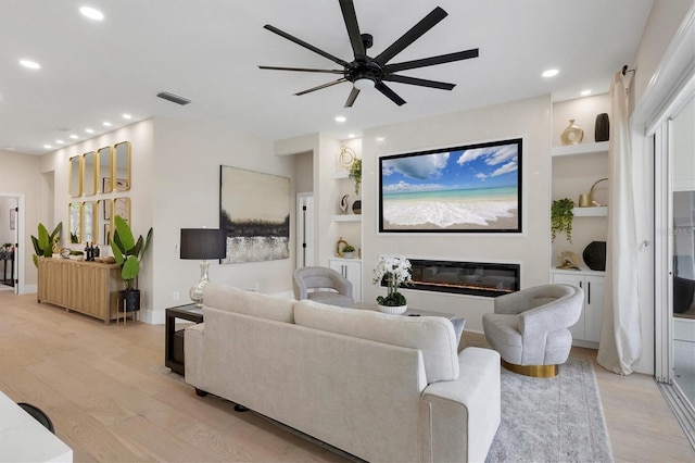 living room featuring ceiling fan, light wood-type flooring, and built in features