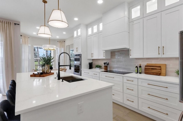 kitchen with decorative light fixtures, white cabinets, black electric cooktop, and an island with sink