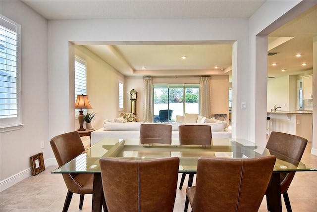 dining room featuring light tile patterned floors, a tray ceiling, sink, and a healthy amount of sunlight