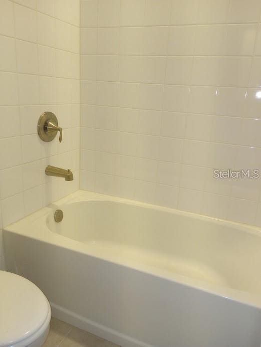 bathroom with tiled shower / bath, tile patterned floors, and toilet