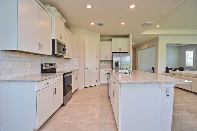 kitchen with appliances with stainless steel finishes, sink, white cabinets, and an island with sink