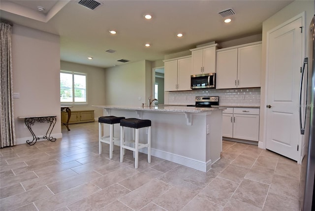 kitchen featuring light stone countertops, white cabinets, a center island with sink, and stainless steel appliances