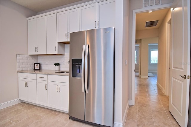 kitchen featuring light stone countertops, white cabinetry, backsplash, stainless steel fridge, and light tile patterned floors