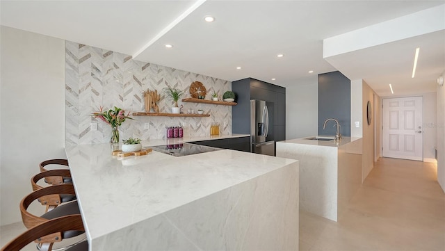 kitchen featuring sink, a kitchen breakfast bar, black electric stovetop, stainless steel fridge with ice dispenser, and kitchen peninsula