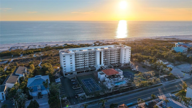 aerial view at dusk featuring a water view and a beach view