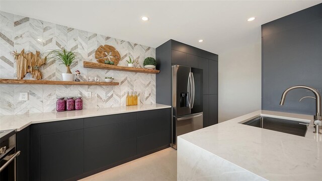 kitchen with light stone counters, stainless steel appliances, sink, and decorative backsplash