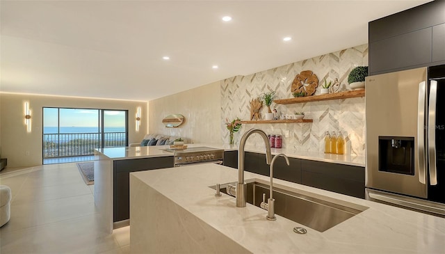 kitchen featuring sink, a water view, tasteful backsplash, light stone counters, and stainless steel appliances