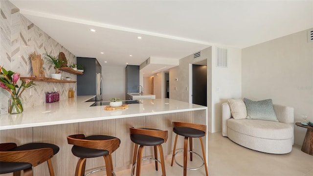 kitchen featuring a breakfast bar, sink, stainless steel fridge, kitchen peninsula, and backsplash