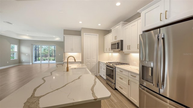 kitchen featuring light stone countertops, appliances with stainless steel finishes, light hardwood / wood-style floors, and white cabinets