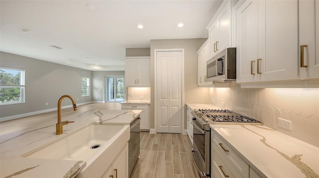 kitchen with sink, stainless steel appliances, white cabinets, and light stone countertops