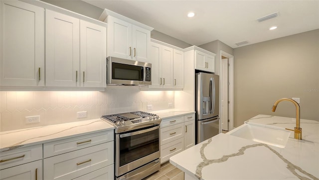 kitchen with sink, white cabinetry, light stone counters, light hardwood / wood-style flooring, and appliances with stainless steel finishes