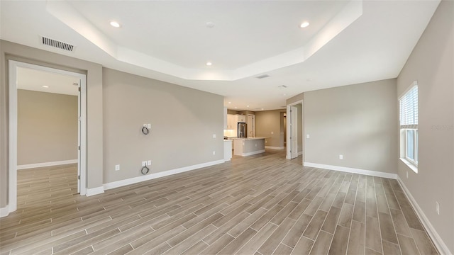 unfurnished living room featuring a tray ceiling and light hardwood / wood-style flooring