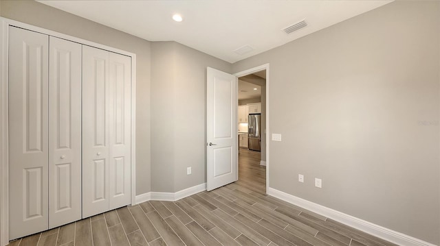 unfurnished bedroom featuring stainless steel fridge, light hardwood / wood-style flooring, and a closet