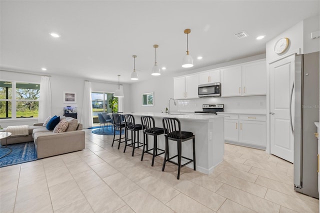 kitchen featuring stainless steel appliances, white cabinetry, hanging light fixtures, and an island with sink